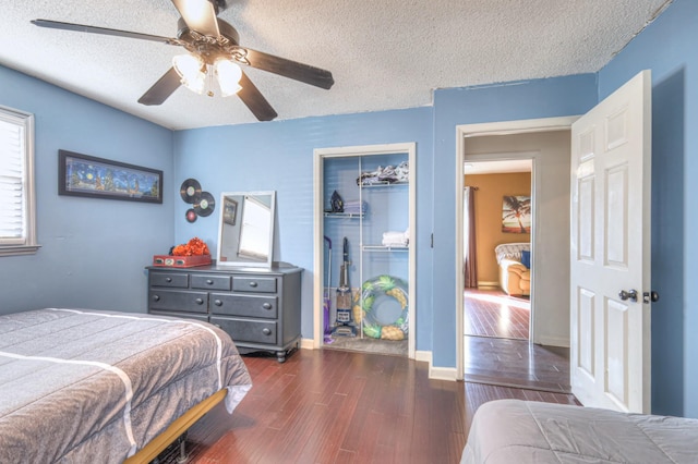 bedroom with a ceiling fan, dark wood-style flooring, a closet, a textured ceiling, and a walk in closet