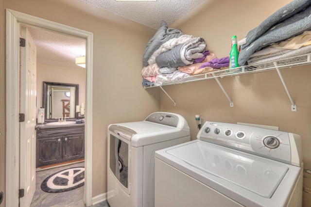 washroom with laundry area, washing machine and dryer, a textured ceiling, and a sink