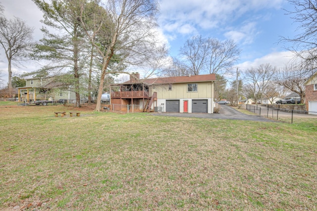 rear view of property featuring fence, driveway, a garage, a lawn, and board and batten siding