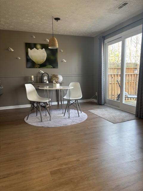 dining room featuring visible vents, baseboards, a textured ceiling, and wood finished floors