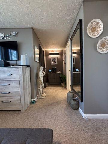 corridor with a textured ceiling, baseboards, and carpet floors