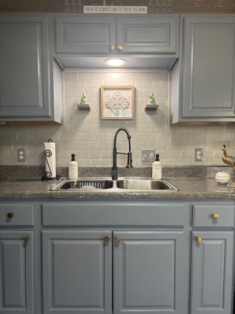 kitchen with a sink, tasteful backsplash, dark countertops, and gray cabinets