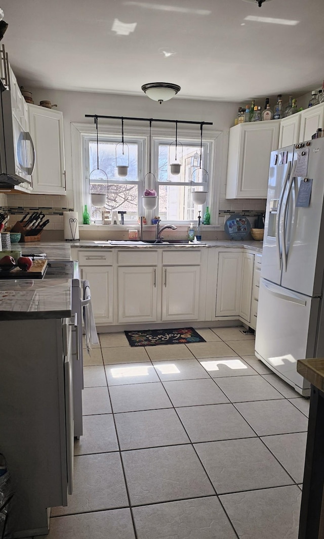 kitchen featuring light tile patterned floors, white refrigerator with ice dispenser, white cabinetry, range, and tasteful backsplash