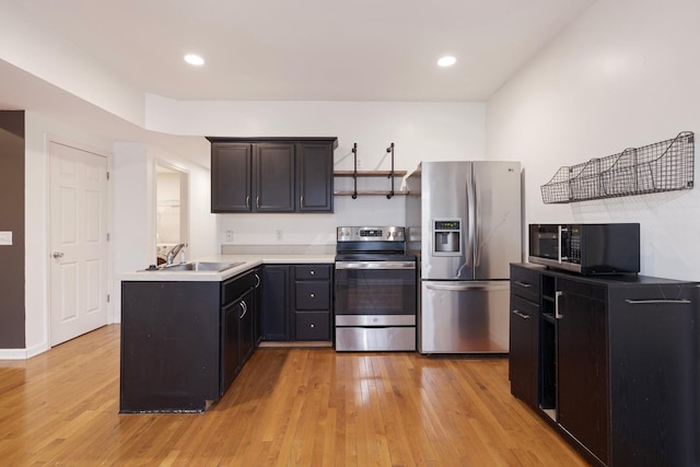 kitchen featuring light countertops, light wood-style flooring, appliances with stainless steel finishes, a peninsula, and a sink