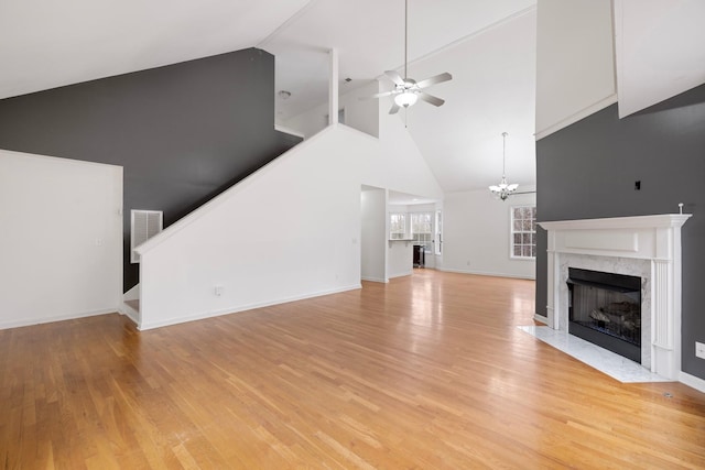 unfurnished living room featuring a high end fireplace, stairway, light wood-style flooring, and ceiling fan with notable chandelier