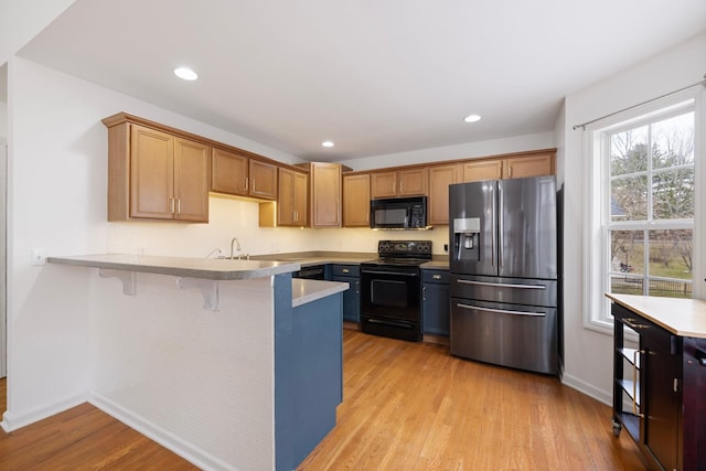 kitchen with black appliances, recessed lighting, light wood-style floors, a peninsula, and light countertops