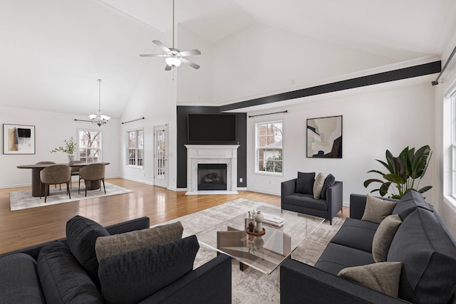 living room with baseboards, light wood finished floors, high vaulted ceiling, a premium fireplace, and ceiling fan with notable chandelier