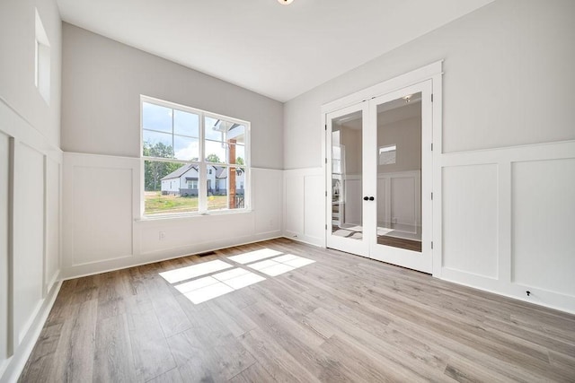 empty room with wood finished floors, a decorative wall, french doors, and a wainscoted wall