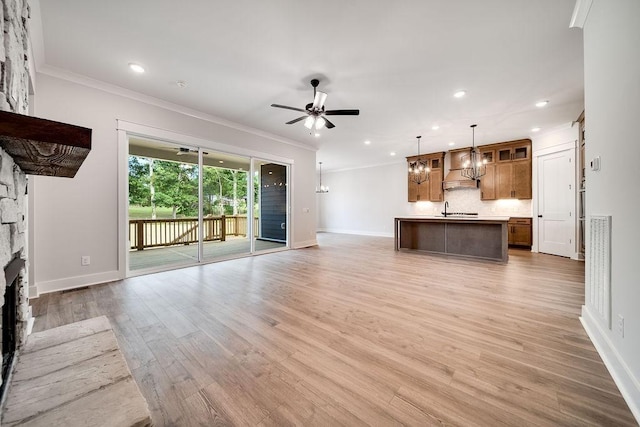 unfurnished living room featuring ceiling fan with notable chandelier, light wood-style floors, a stone fireplace, crown molding, and baseboards