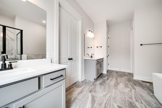 bathroom with a stall shower, two vanities, baseboards, and a sink