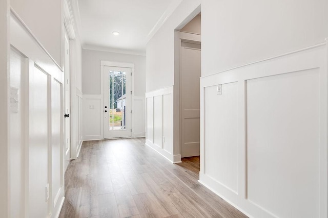 entryway with light wood-style floors, ornamental molding, wainscoting, and a decorative wall