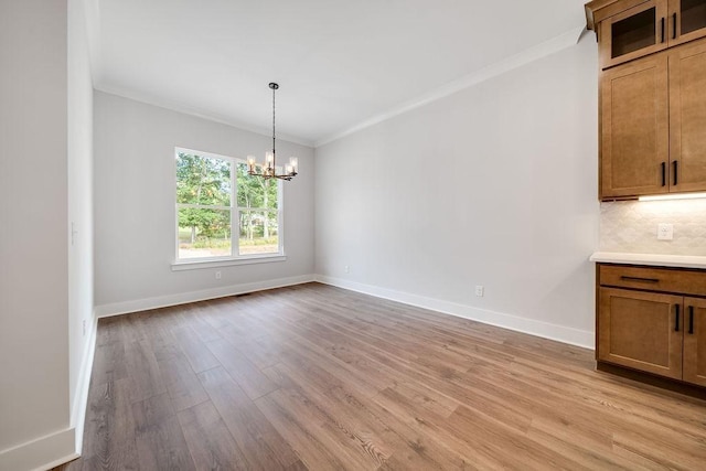 unfurnished dining area with a chandelier, light wood-style floors, and ornamental molding