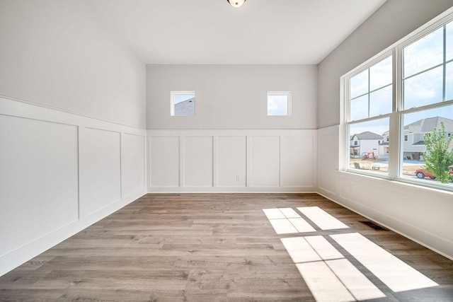 empty room featuring light wood finished floors, visible vents, a decorative wall, and a wainscoted wall