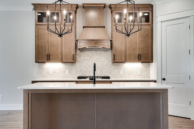 kitchen with custom exhaust hood, a notable chandelier, light countertops, and a kitchen island with sink