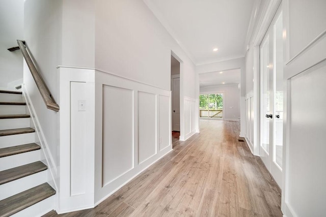 corridor with recessed lighting, a decorative wall, wainscoting, light wood finished floors, and stairs