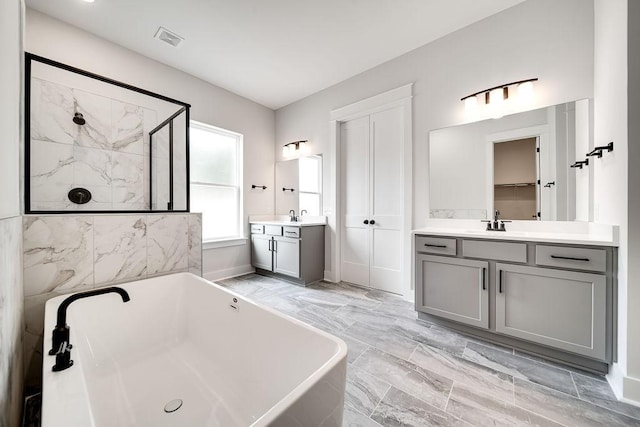 full bath featuring visible vents, a shower stall, two vanities, a freestanding tub, and a sink