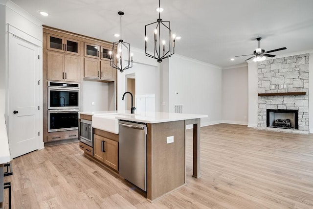 kitchen featuring light wood-type flooring, ornamental molding, stainless steel appliances, a stone fireplace, and light countertops