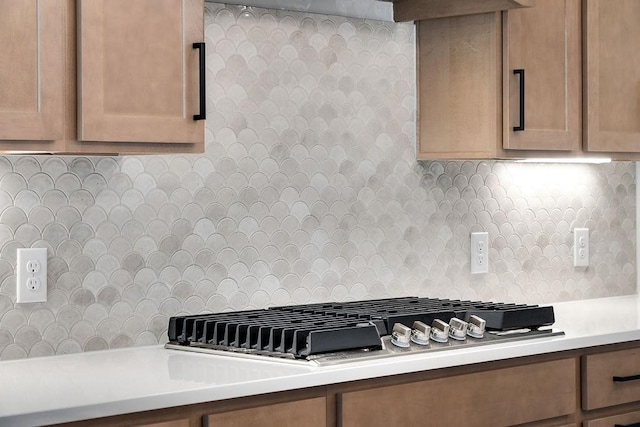 kitchen featuring stainless steel gas cooktop, backsplash, brown cabinetry, and light countertops