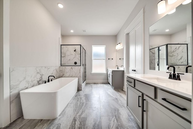 full bathroom featuring a shower stall, a freestanding bath, two vanities, marble finish floor, and a sink