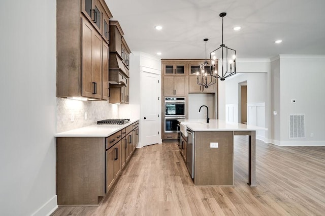 kitchen featuring visible vents, backsplash, an island with sink, light wood-type flooring, and stainless steel appliances