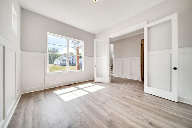 unfurnished bedroom with wainscoting, visible vents, light wood-style flooring, and a decorative wall