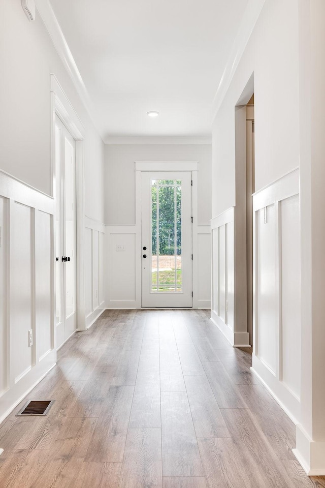 doorway to outside featuring visible vents, wood finished floors, crown molding, and a decorative wall