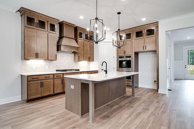 kitchen featuring a center island with sink, custom range hood, tasteful backsplash, stovetop, and crown molding