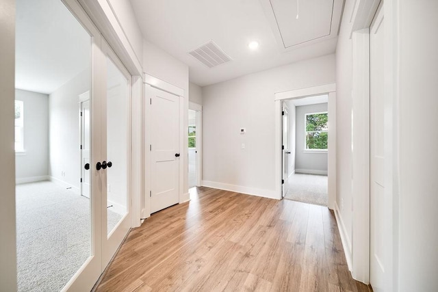 hall with visible vents, baseboards, attic access, and light wood-style flooring