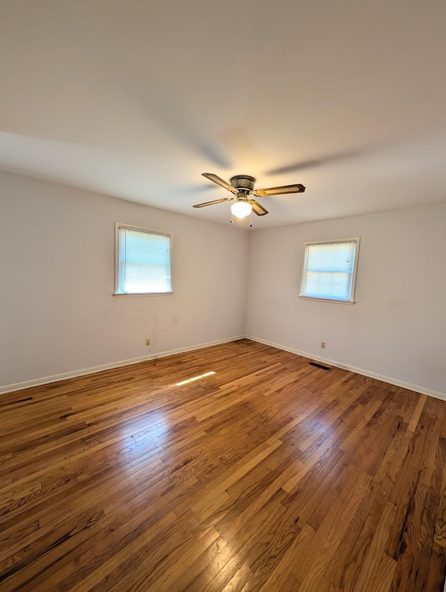 empty room featuring plenty of natural light, wood finished floors, visible vents, and baseboards