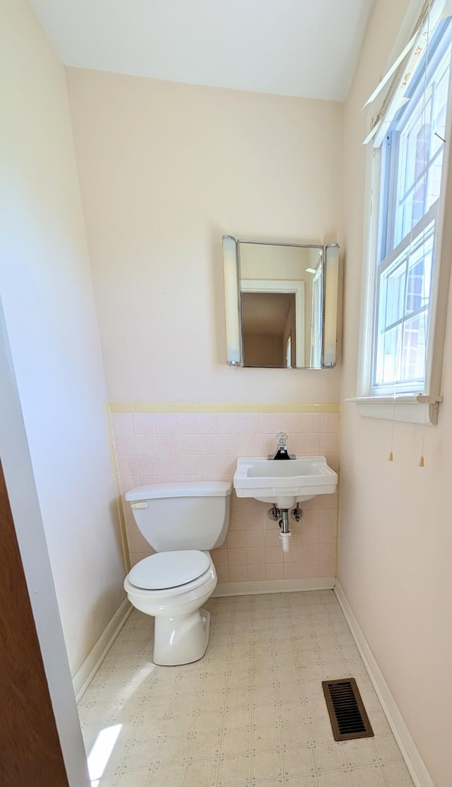 bathroom featuring a wainscoted wall, visible vents, a sink, tile walls, and toilet