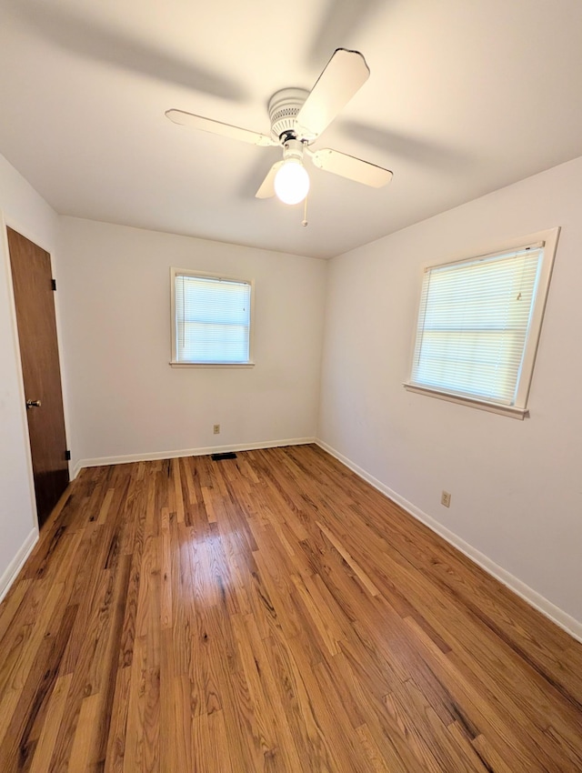 unfurnished bedroom with multiple windows, wood finished floors, baseboards, and ceiling fan