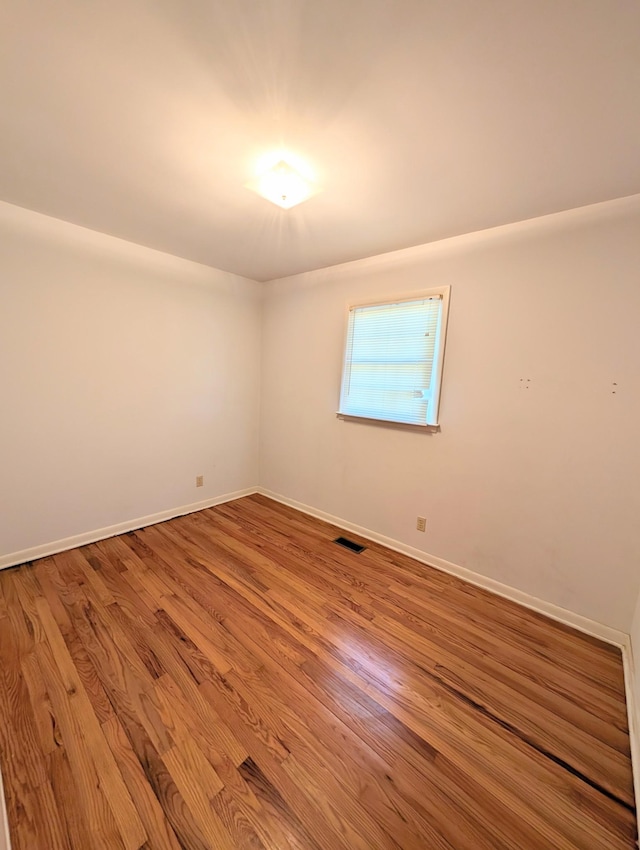 unfurnished room with wood finished floors, visible vents, and baseboards