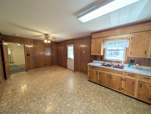 kitchen featuring brown cabinets, a ceiling fan, a sink, wooden walls, and light countertops