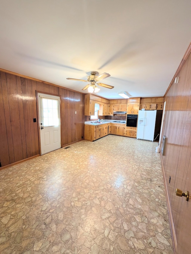 kitchen featuring wooden walls, brown cabinetry, white refrigerator with ice dispenser, stone finish flooring, and black oven