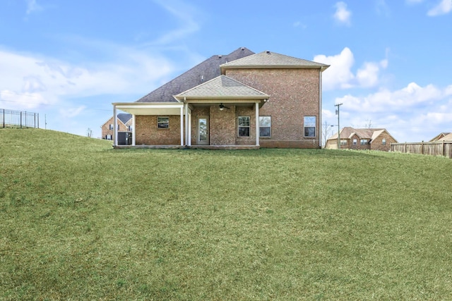 rear view of house featuring a yard, brick siding, roof with shingles, and ceiling fan