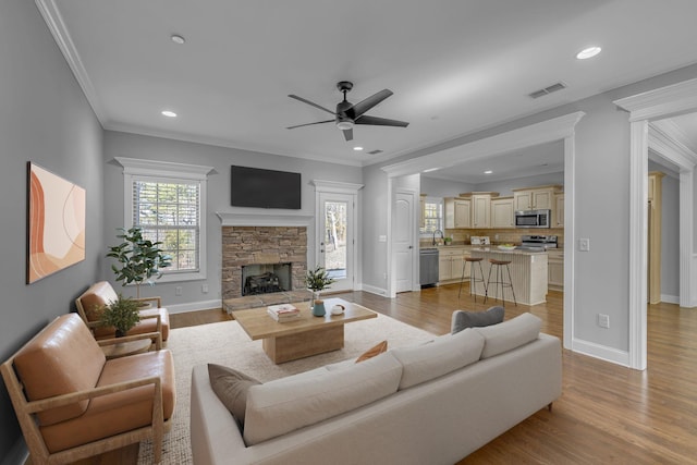 living area with visible vents, ornamental molding, light wood-style floors, a stone fireplace, and baseboards