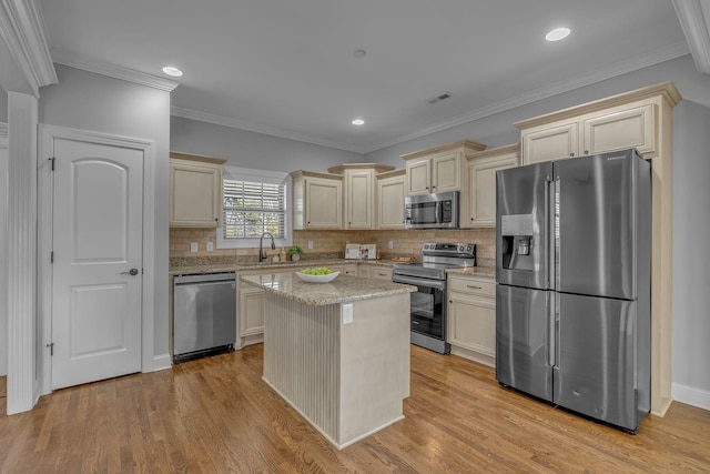 kitchen with light wood finished floors, decorative backsplash, cream cabinetry, stainless steel appliances, and a sink