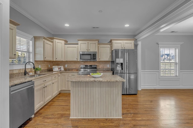 kitchen with a sink, cream cabinets, appliances with stainless steel finishes, light wood finished floors, and light stone countertops