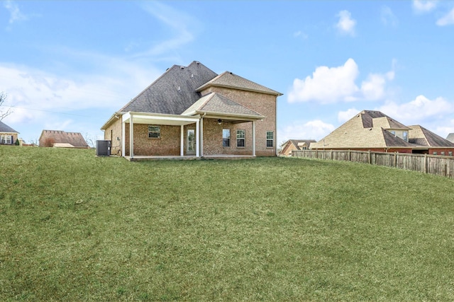 rear view of house with a ceiling fan, fence, central AC unit, a shingled roof, and a lawn