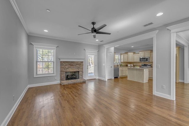 unfurnished living room featuring visible vents, baseboards, ornamental molding, a fireplace, and wood finished floors