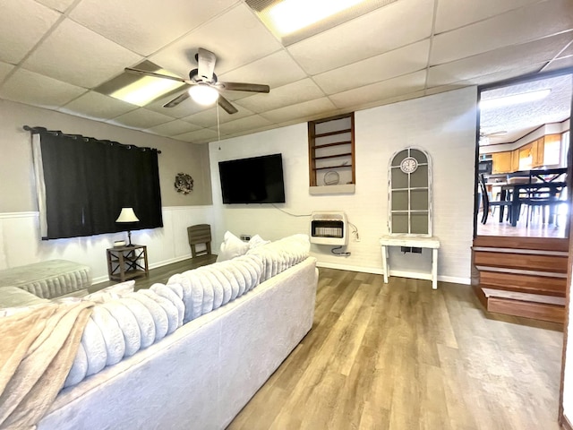 living area featuring heating unit, a ceiling fan, wood finished floors, a wainscoted wall, and a paneled ceiling