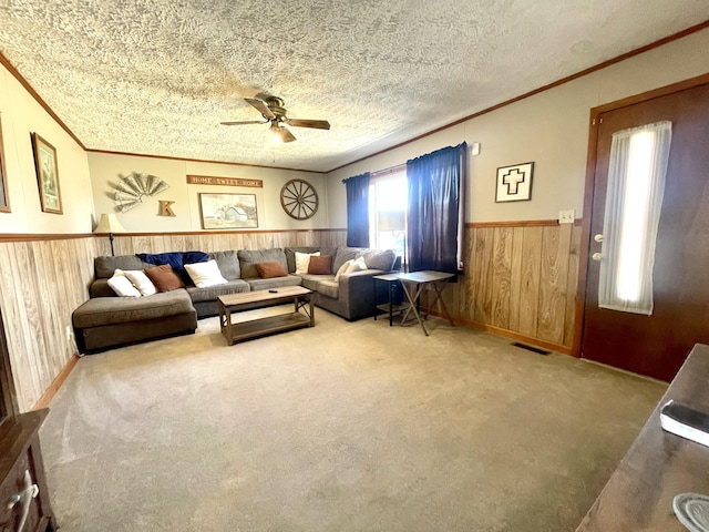 carpeted living room with a wainscoted wall, visible vents, a textured ceiling, wooden walls, and crown molding