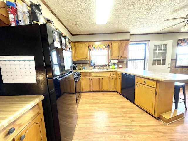 kitchen featuring black appliances, a peninsula, light countertops, and a sink