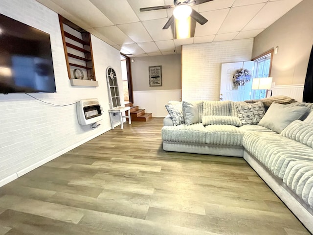 living area featuring heating unit, a ceiling fan, wood finished floors, a drop ceiling, and wainscoting