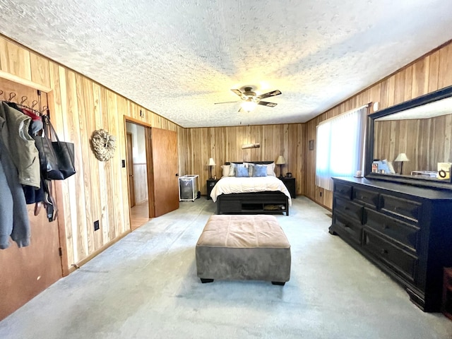 bedroom with wooden walls, light colored carpet, a textured ceiling, and a ceiling fan