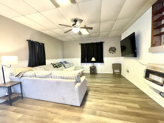 living room featuring a ceiling fan, heating unit, wood finished floors, wainscoting, and a paneled ceiling