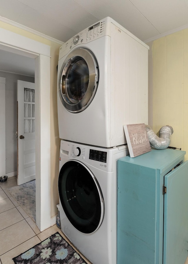 laundry area with stacked washer and dryer, light tile patterned flooring, laundry area, and crown molding