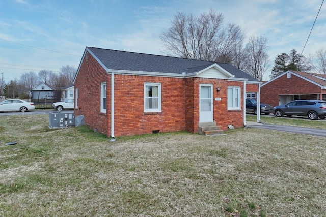 bungalow-style house with brick siding, entry steps, a front yard, and roof with shingles