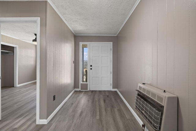 entryway with heating unit, a textured ceiling, wood finished floors, crown molding, and baseboards