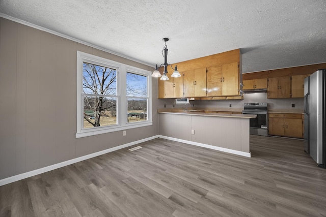 kitchen with under cabinet range hood, wood finished floors, a peninsula, appliances with stainless steel finishes, and brown cabinetry